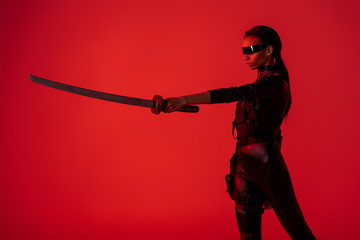 futuristic african american woman in glasses with sword on red background