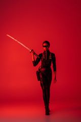 futuristic african american woman in glasses walking with sword on red background © LIGHTFIELD STUDIOS
