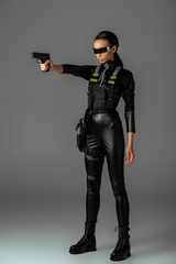Fototapeta premium attractive futuristic african american woman in glasses aiming gun on grey