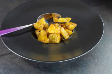 Ananas rôti à la vanille cuisiné en salade de fruit dans une assiette noire creuse avec une cuillère au manche dégradé violet