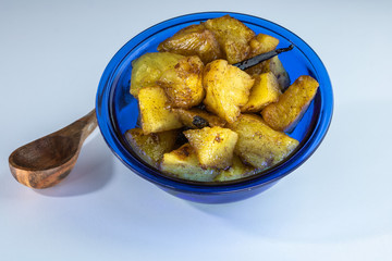 Ananas rôti à la vanille de bourbon dans un ramequin en verre bleu avec une cuillère en bois sur fond blanc