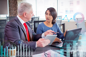 Two business colleagues working together in meeting space with virtual statistic diagrams. Young...