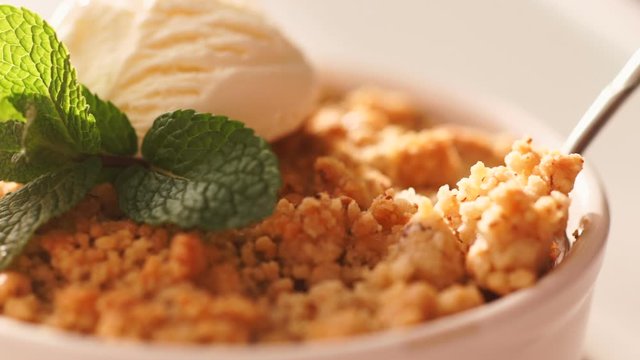 Close up of an apple crumble with vanilla ice cream is taken with a dessert on a fork. Classical english autumn comfort food.
