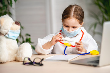 Pretty little girl dressed in a white lab coat and mask was taking the temperature of a Teddy bear.