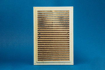 Dirty and dusty plastic ventilation grill for the home on a blue background.