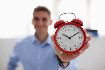 Smiling business woman holding in hand on the alarm clock a red color showing ten o'clock in the morning or evening AM PM