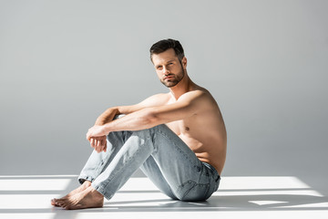 sunlight on muscular man in blue jeans sitting on grey