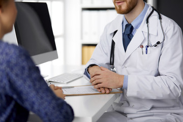 Unknown red-bearded doctor and patient woman discussing current health examination while sitting in...