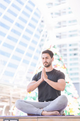 Fototapeta na wymiar An Iranian man dressed in casual clothes, he was sitting cross-legged and with his hands clinging to a tall building in the morning. In the concept of exercise and yoga