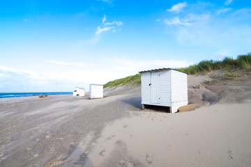 Obraz na płótnie Canvas Small white locker house at the North Sea beach in the Netherlands. The blue sky is interspersed with clouds.
