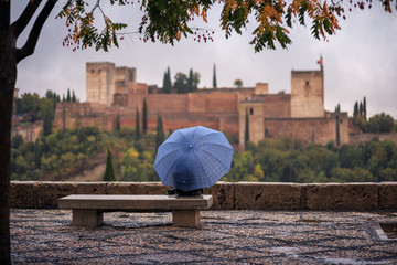 Tourist with umbrellas looking at the Alhambra from the Mirador de San Nicolas, a rainy day.