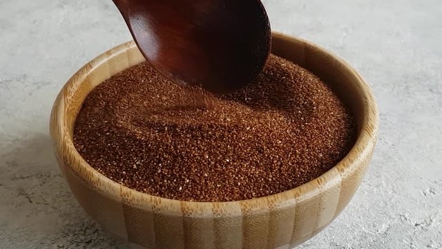 Uncooked teff grain in a bowl with a wooden spoon close up