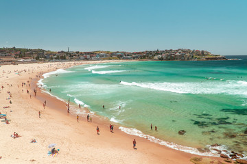 Bondi Beach Sydney holiday scene. Famous vacation spot in city, with beautiful ocean, sun, sea and sand. Tourists sunbathing on beach, with waves washing in. Australia.