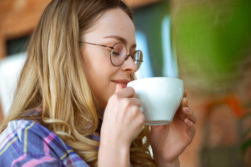 Close up of beautiful joyful woman drinking coffee at home. Enjoying her break. Concept of working, studying at home, domestic life. Home comfort, quarantine, isolation. Aroma hot tasty drink.