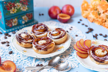 gebackene Blätterteigrosen mit Pflaumen und Puderzucker auf  hellen blauen Brettern aus Holz im nostalgischen Stil wie früher bei Oma