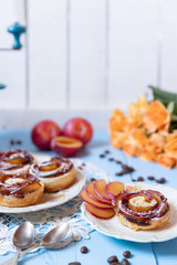 gebackene Blätterteigrosen mit Pflaumen und Puderzucker auf  hellen blauen Brettern aus Holz im nostalgischen Stil wie früher bei Oma