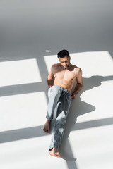 Fototapeta premium sunshine on muscular man in blue jeans sitting on grey