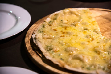 Pizza quattro formaggio with four kinds of cheese: mozzarella, parmesan, dorblue and gorgonzola on round wooden plate and two white plates on the table. Friends party in restaurant. People in restaura