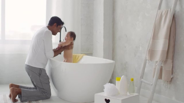 Handheld shot of happy Indian father doing Eskimo kisses to adorable toddler girl taking bath in morning