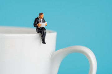 business miniature figures sitting and read a book, read newspaper, waiting, talking and relax on white cup of hot coffee..