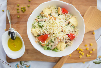 Bowl of Traditional Caesar Salad with Chicken and Bacon . Chicken Fillet and Parmesan Cheese . Peas. Corn kernels. olives on a small white bowl . Caesar salad on table - Healthy food style .