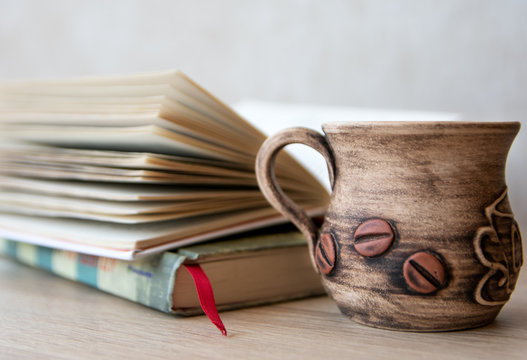 Сup of coffee with books on the table. 
Books and cup of coffee or tea on a wooden table. 
Cup of coffee or tea with open book on the table.