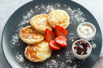 Tasty cheese pancakes with strawberries, sour cream and cherry jam. Cheese pancakes on a plate
