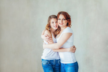 Obraz na płótnie Canvas Stay at home mom, stay safe. Young mother embracing her child. Woman and teenage girl relaxing in white bedroom near gray wall indoors. Happy family at home. Young mom playing whith her daughter.
