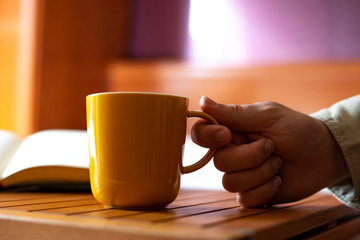 Hand picking up a yellow cup of coffee at home.
