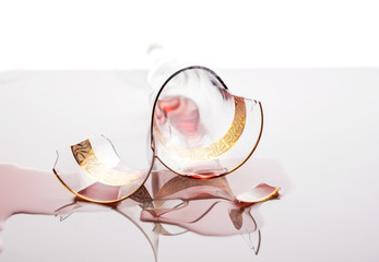 A broken glass with droplets of wine lies on a light background.