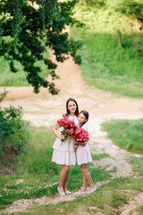 Two sisters dressed in white dresses have fun summertime together. Girls are holding flowers.