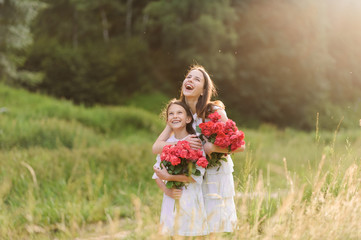 Two sisters dressed in white dresses have fun summertime together. Girls are holding flowers.