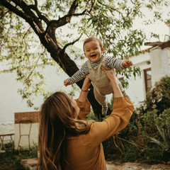 Mother holding her baby son up in the air, and baby laughing. - 339890600