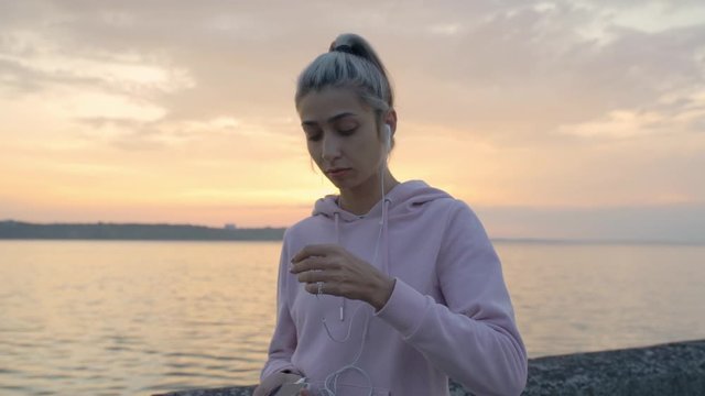 Young girl in headphones runs on a background of sunset and water, slow motion
