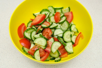 vegetable salad of fresh tomatoes and cucumbers in a yellow salad bowl