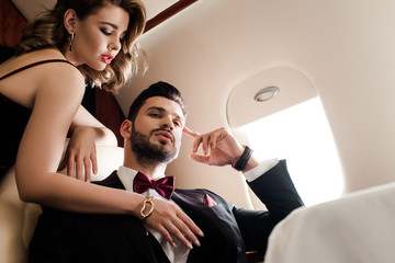 low angle view of sexy woman touching chest of elegant, confident man in plane