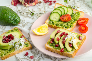 Fototapeta na wymiar sandwich with avocado, pomegranate and tomato and green smoothie on a white table. Vegan Breakfast and Healthy Slimming Nutrition