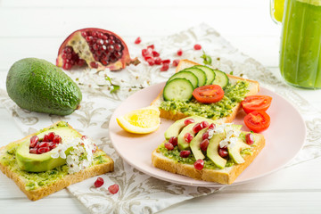 
sandwich with avocado, pomegranate and tomato and green smoothie on a white table. Vegan Breakfast and Healthy Slimming Nutrition