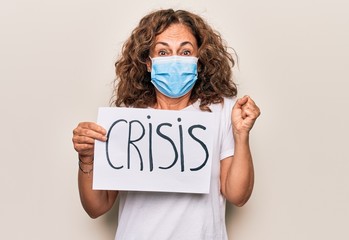 Middle age woman wearing coronavirus protection mask holding epidemic crisis paper as protest screaming proud, celebrating victory and success very excited with raised arm