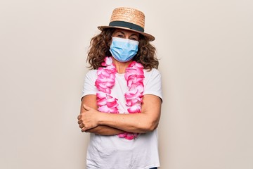 Middle age tourist woman wearing coronavirus protection mask and summer hat on vacation happy face smiling with crossed arms looking at the camera. Positive person.