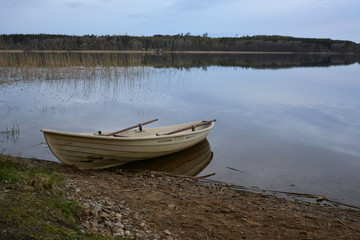 A rowing boat at the waterfront of mirror water surface with dark forest on the background.