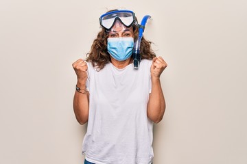 Middle age woman wearing coronavirus protection mask and diving gogles glasses as canceled vacation screaming proud, celebrating victory and success very excited with raised arm