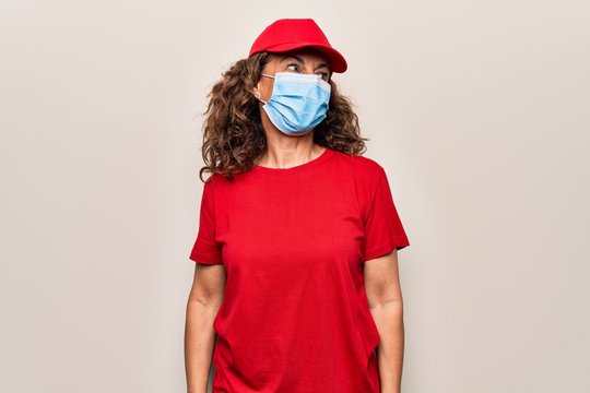 Middle Age Delivery Woman Wearing Red Cap And Coronavirus Protection Mask Looking To Side, Relax Profile Pose With Natural Face And Confident Smile.