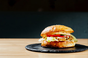 Chicken steak burger with tomatos on black plate. Junk food. Fastfood. Bodypositive. Food on quarantine from delivery. Photo for menu.