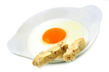 Un œuf au plat avec des mouillettes dans une assiette sur fond blanc