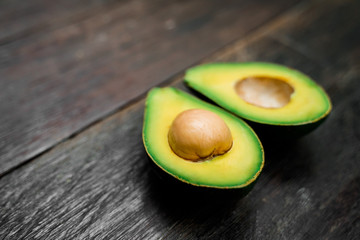 A side view of a ripe avocado halves lying on a wooden brown background with copy space. One slice...
