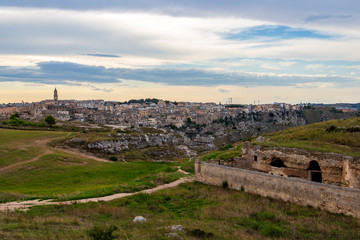 Fototapeta premium Parco della Murgia Materana or Park of the Rupestrian Churches of Matera with ancient architecture, distant panoramic view of Matera in the backgrond. Province of Matera, Basilicata Region, Italy at s