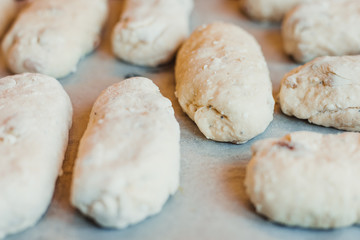 A lots raw curd buns with raisins lie on a baking sheet. Raw dough. Unbaked buns. Selective focus