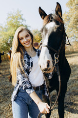 Obraz premium Portrait of beautiful young woman smiling and standing by horse in countryside. 