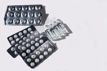 Different medicines: white plain breakable tablets in transparent sticks, in metal non-trasparent sticks and ampuls with anti-virus vaccine on white background. Copy space.